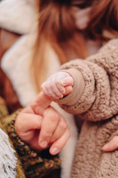 Close-up of a baby holding an adult's finger in a cozy setting, symbolizing love and connection.