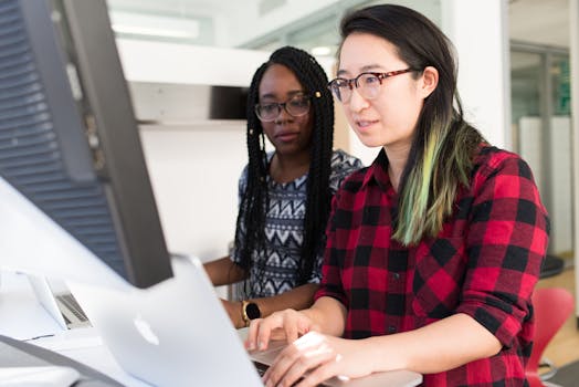 Two women working on a computer project together in an office setting.