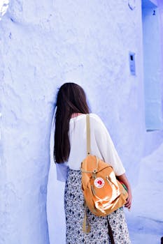 Young woman leans against blue wall in Chefchaouen, Morocco, with a backpack.