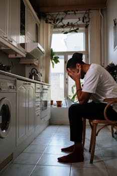 A man sits in a kitchen, deep in thought, illustrating emotions and solitude.