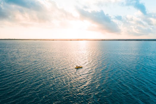 A peaceful scene of a lone kayaker gliding across a vast ocean under a vibrant sunrise.