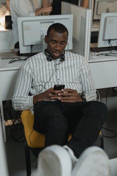 An office worker seated comfortably while using a smartphone, with a focus on relaxation and multitasking.