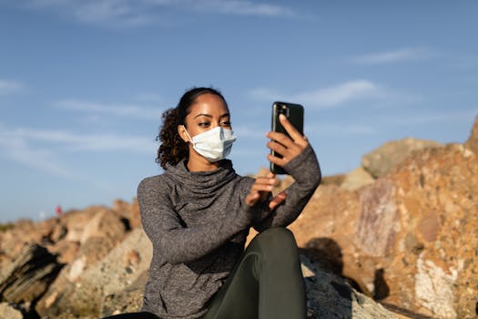 Woman in a face mask takes a selfie in a rocky outdoor setting, capturing a sunny day moment.